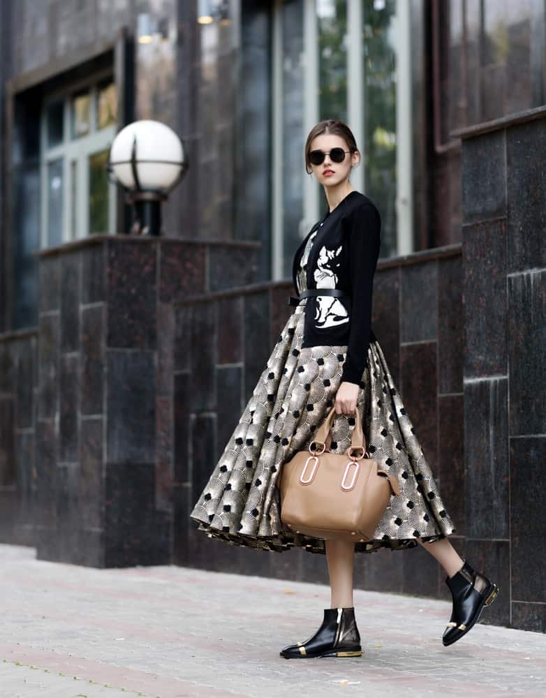 Model in a girly dress holding a leather bag.