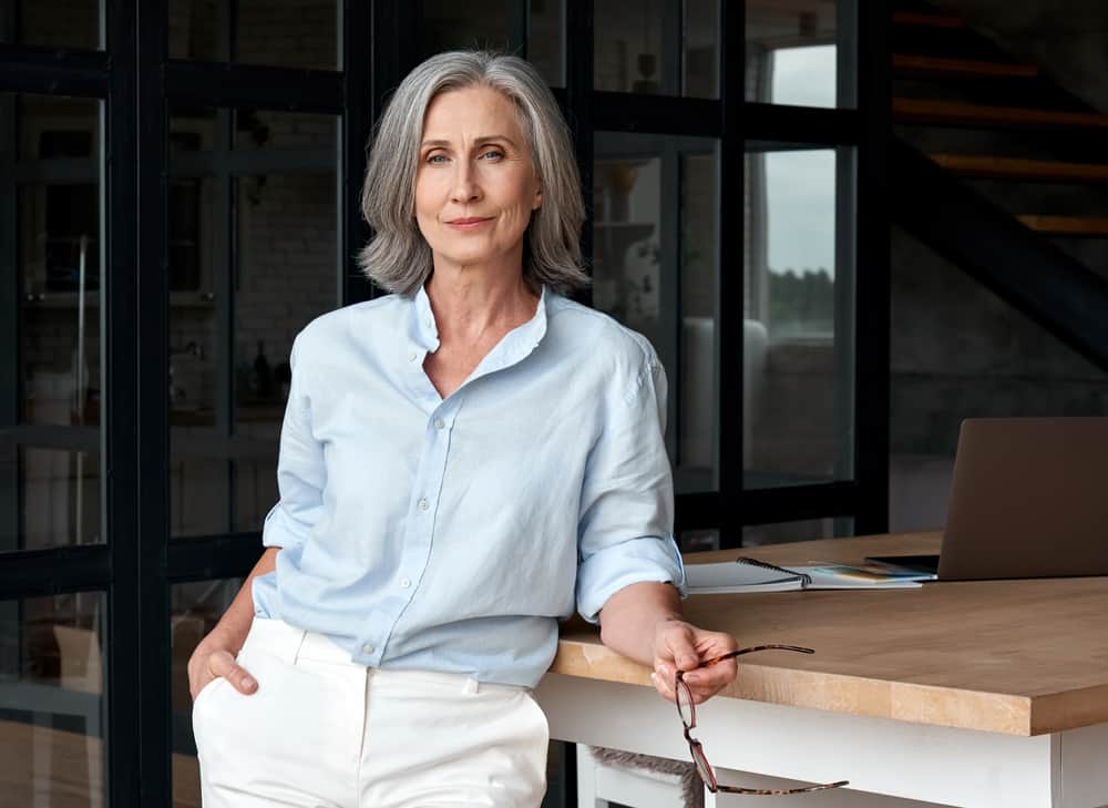 Woman in a minimalist outfit leaning on a wooden desk.