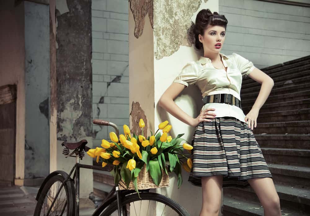 Retro lady posing against a pillar next to a bike.
