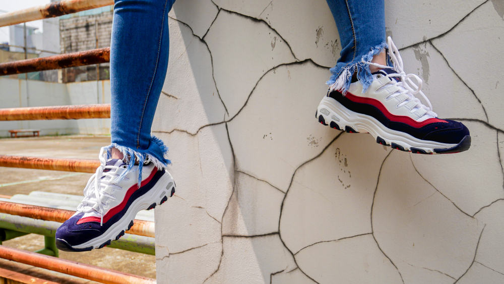 This is a close look at a man wearing a pair of Skecher sneakers with his ripped jeans.