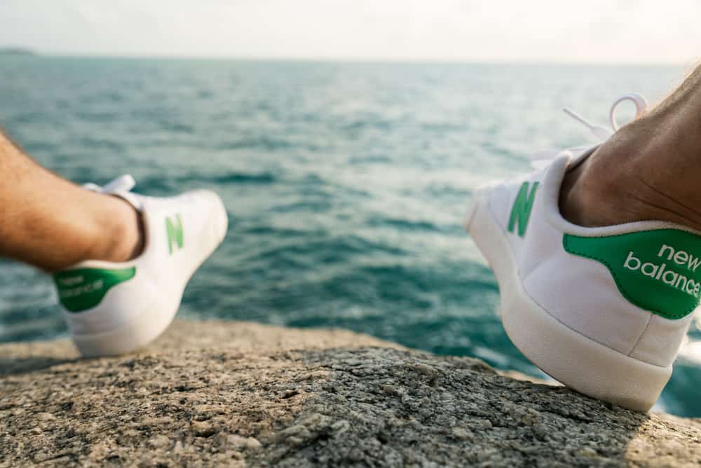 This is a close look at a man wearing a pair of New Balance sneakers by the sea.