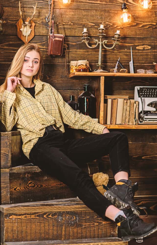 Woman wearing plaid top sitting on wooden stairs.
