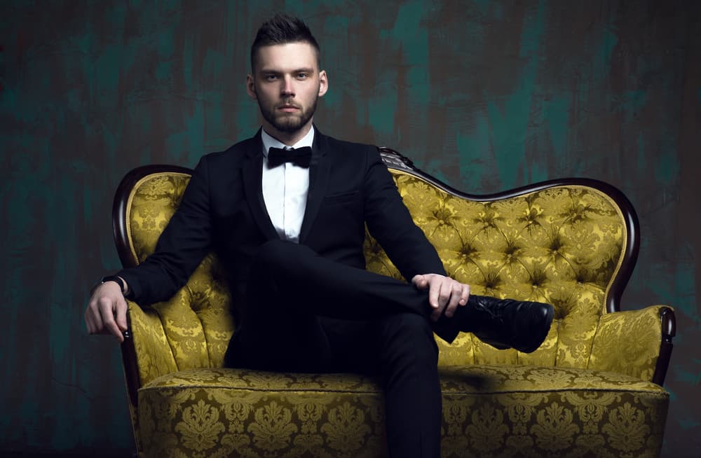 Man in his tuxedo sitting on a classy couch.