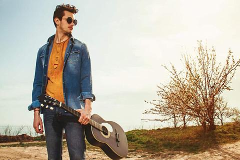 Man in bohemian clothes poses with guitar in his hands.