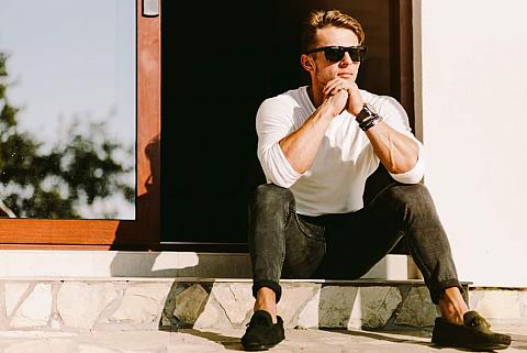 Man in casual outfit and shades sitting outside his house.