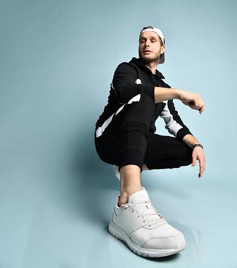 Man wearing black tracksuit, white sneakers, and a matching cap.