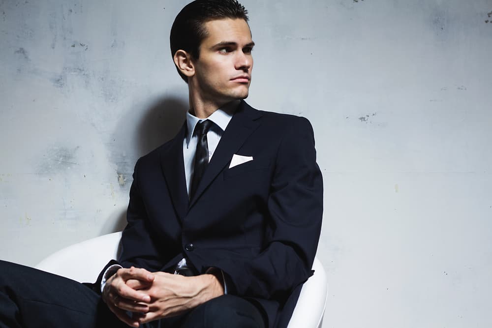 man in a black business suit sitting on a white chair