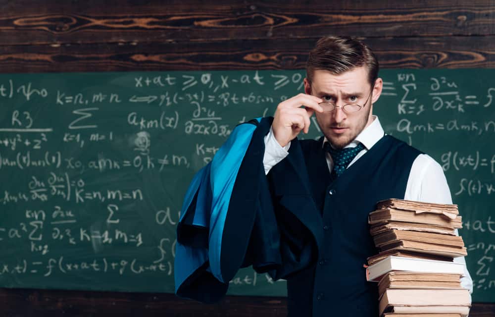 Professor holding a pile of books as he looks over his glasses.