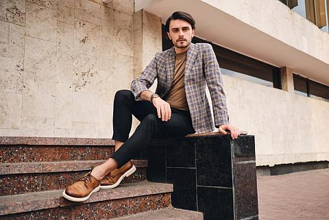 Young man in checkered jacket sitting outdoors.