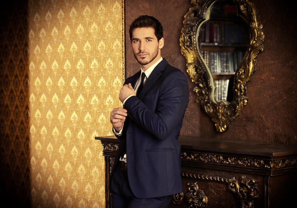 Man in formal coat standing inside a classic interior.
