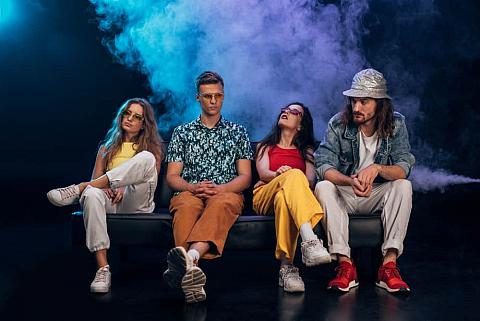 Group of friends sitting on couch in nightclub during rave party.