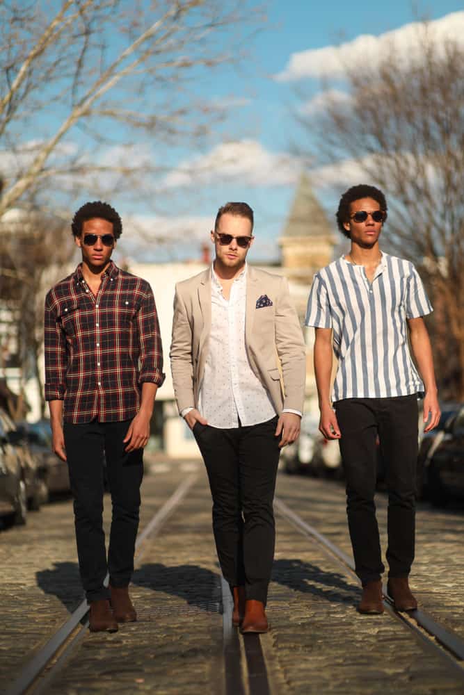 A group of men in streetwear walk down a cobblestone street.