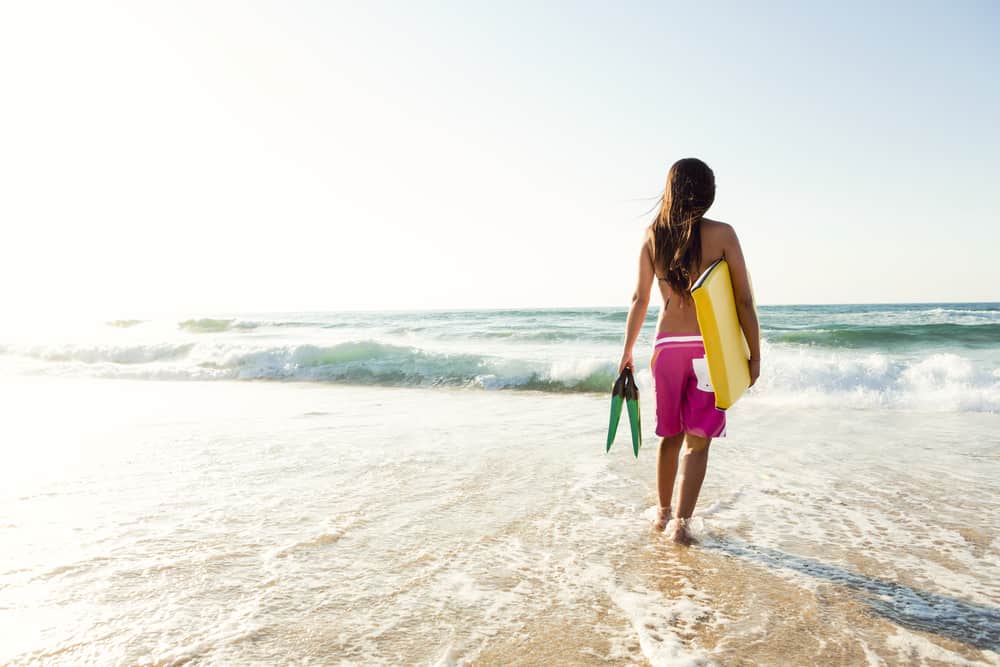 A woman wearing a pair of pink board shorts about to go surfing.