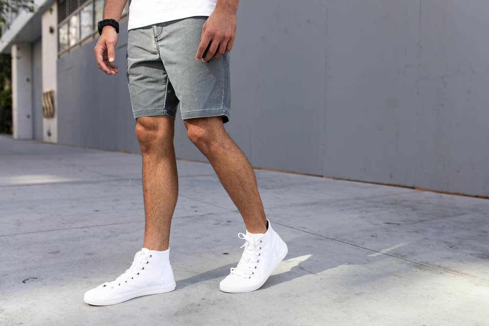 This is a close look at a man wearing ankle-high sneakers with his denim shorts.