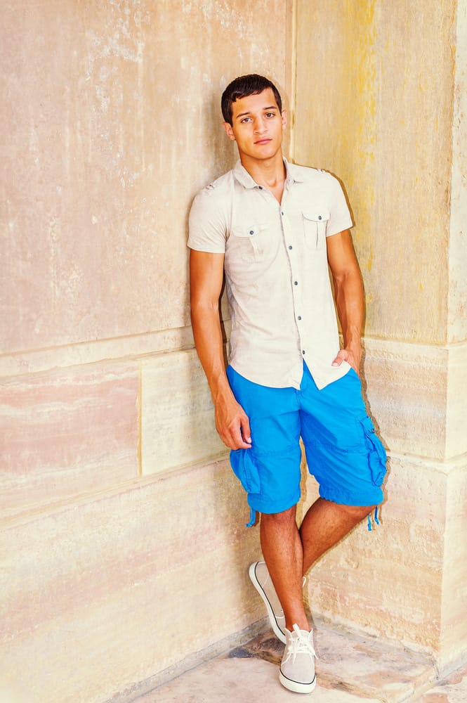 A man wearing a pair of long blue cargo shorts with his sneakers.
