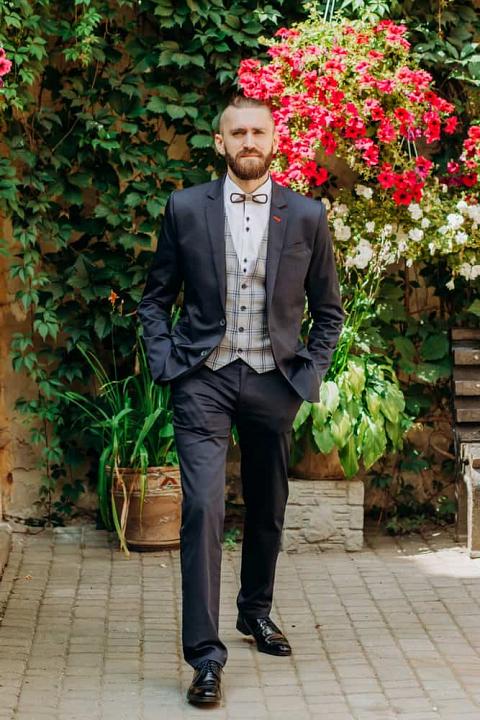 Man in white tie dress standing against the floral backdrop.