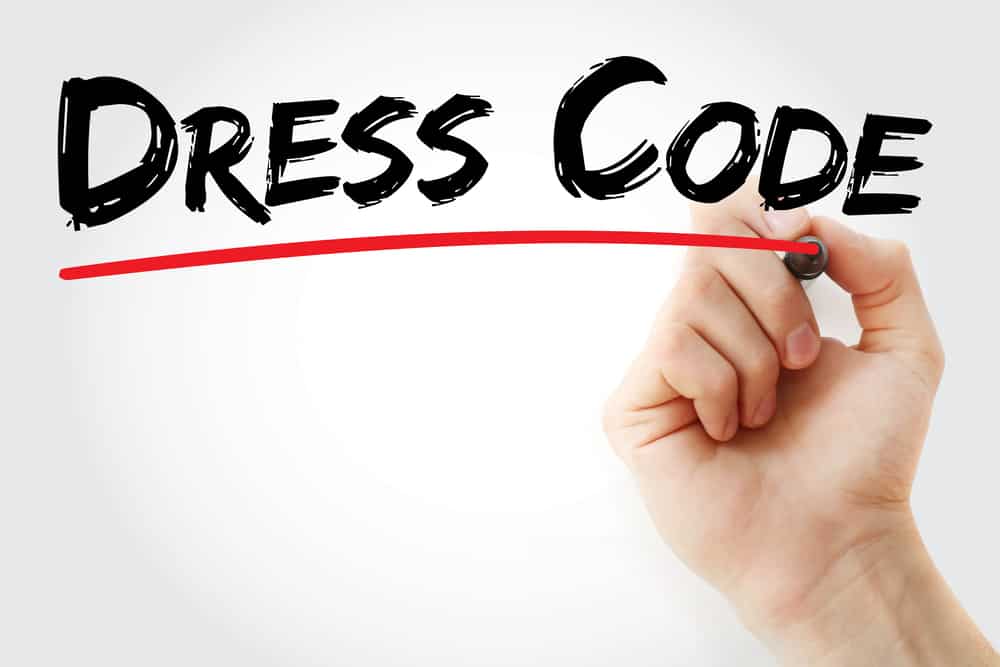 This is a hand writing the words Dress Code with a red underline.