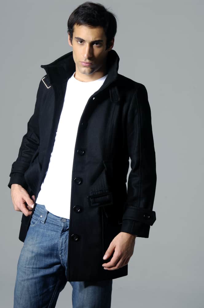 A man wearing a black jacket over his white shirt and denim jeans.