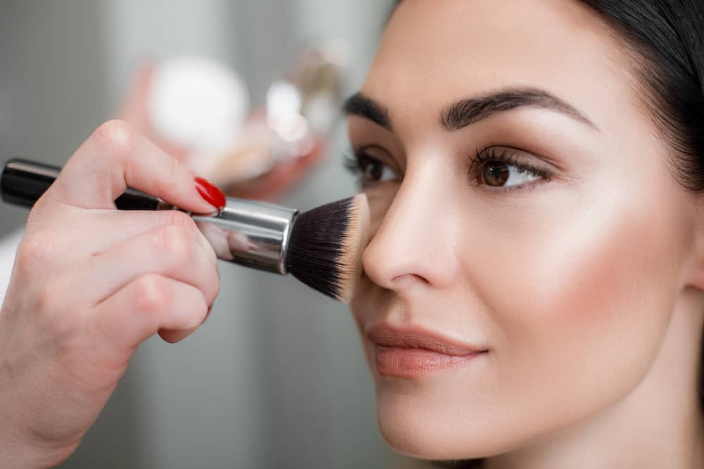 Makeup artist applying light layer of matting powder on a woman's face.
