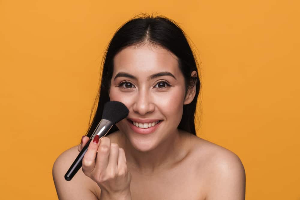 Woman applying primer with makeup brush.