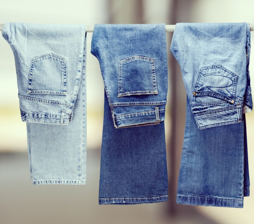 Three denim jeans hanging on a white rod.