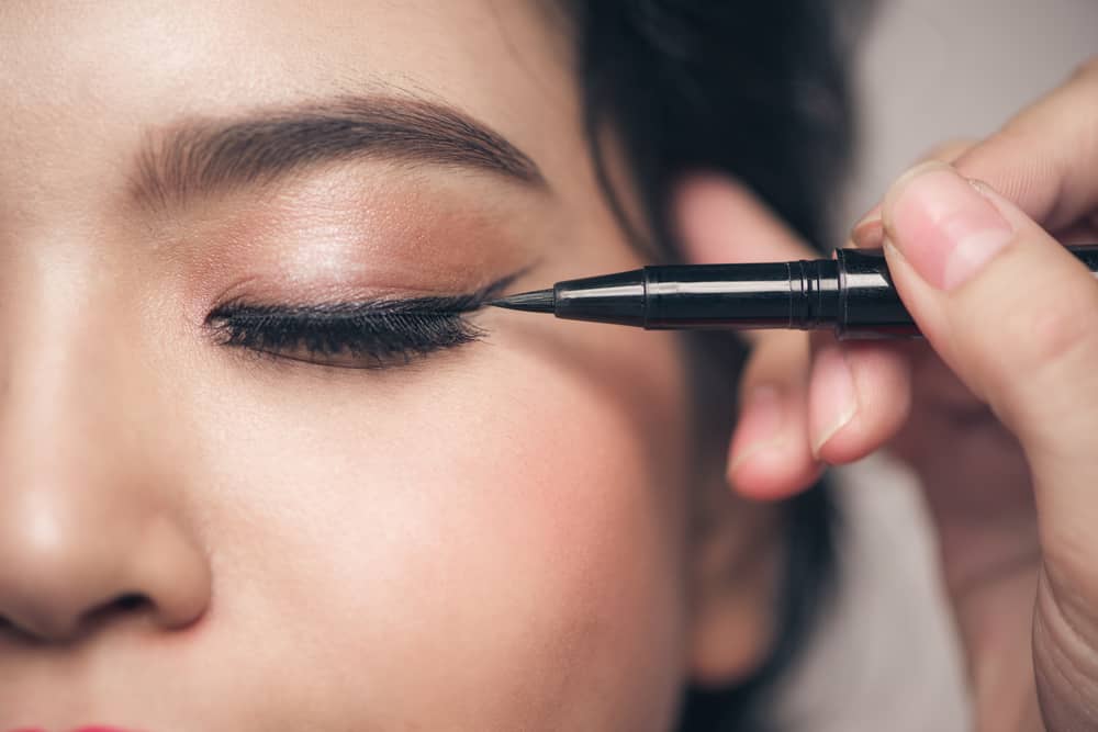 Close-up portrait of a woman with eyeliner on her closed eyes.