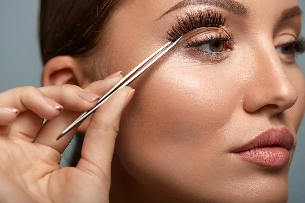 Woman applying false eyelashes with tweezers.