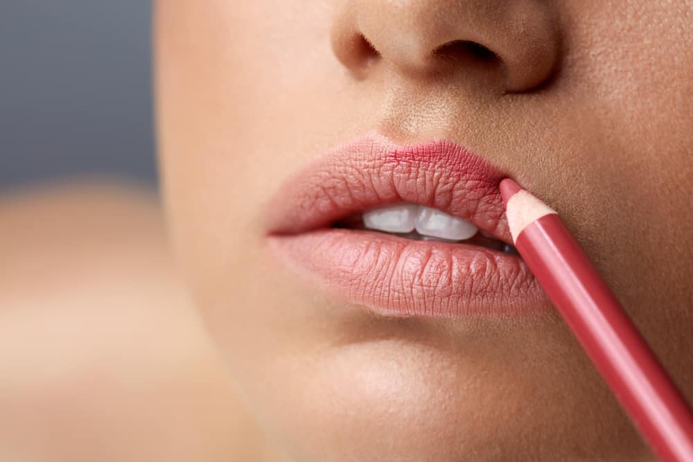 Woman contouring lips using lip liner.