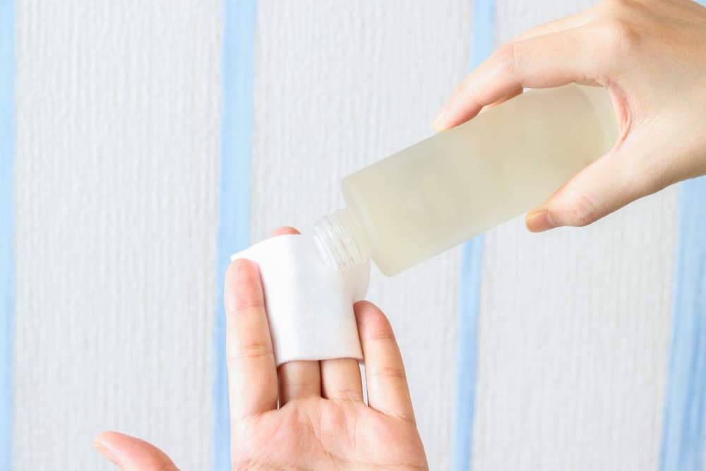 Hands applying toner on a cotton pad.