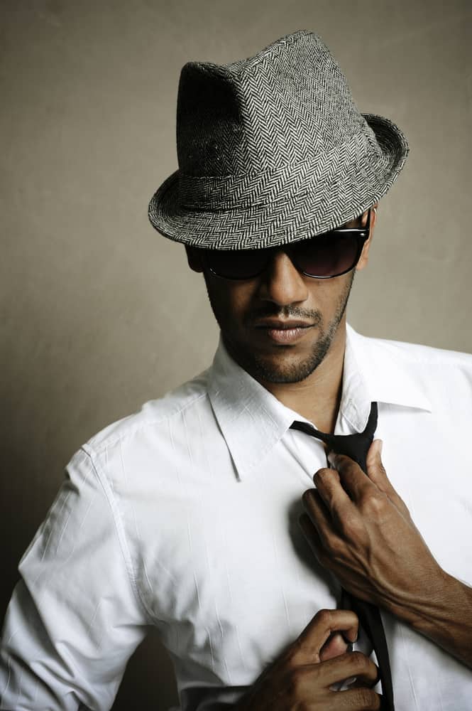 A man wearing a gray fedora with his white button-down shirt and tie.