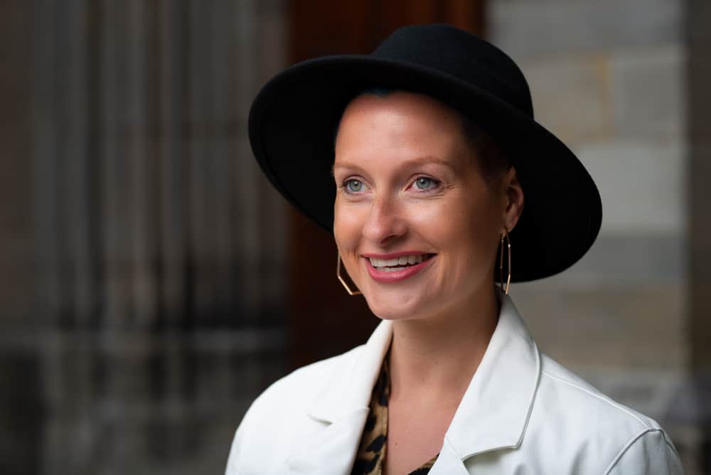 A woman wearing a black fedora with her white coat.