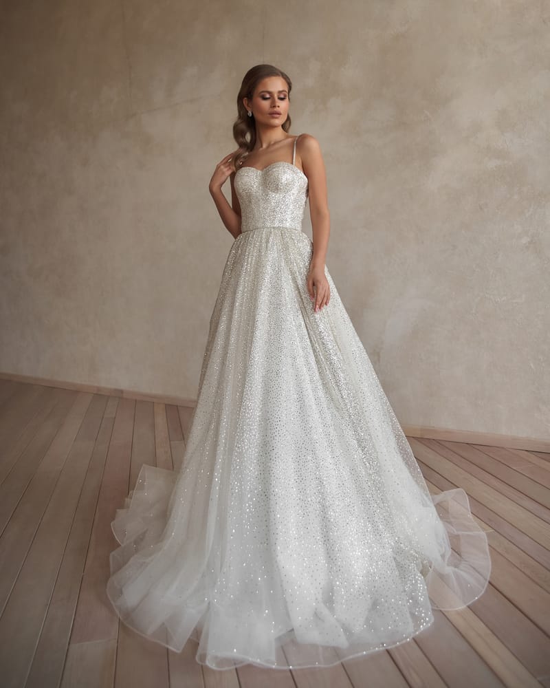 Bride in a beaded wedding gown poses against the concrete wall.