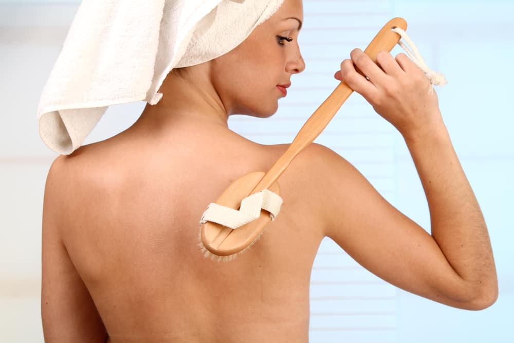 A woman using a back scrubber with handle.