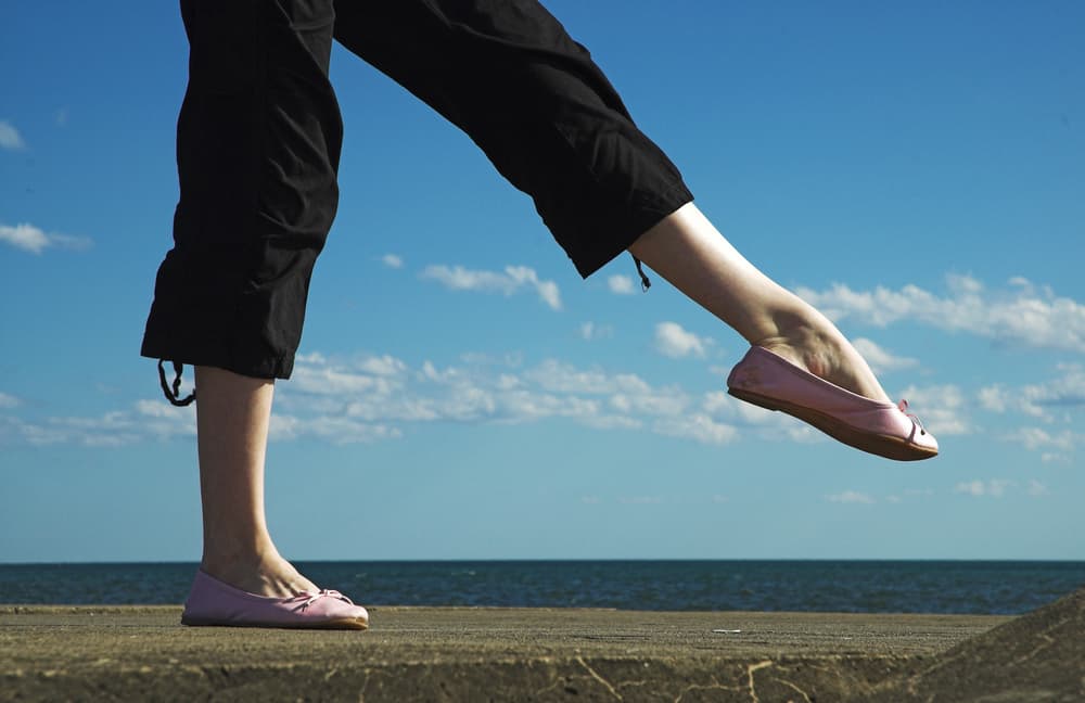 This is a close look at a woman wearing a pair of black carpi pants and a pair of pink flats.