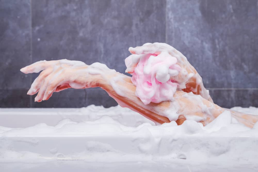 A woman using a bath sponge at the bathtub.
