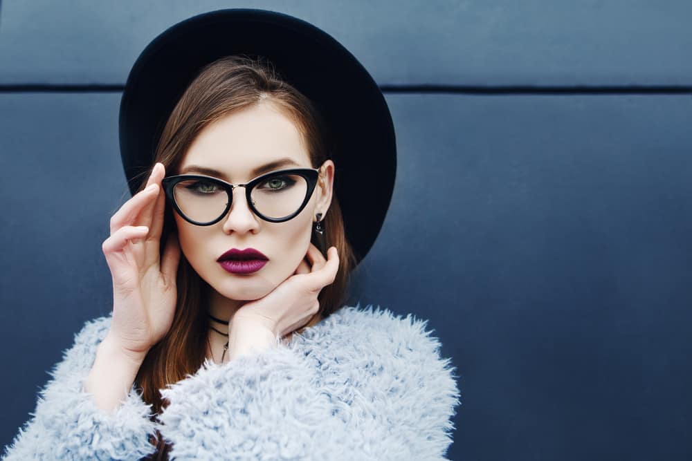 A woman wearing a fur coat, glasses and a fedora hat.