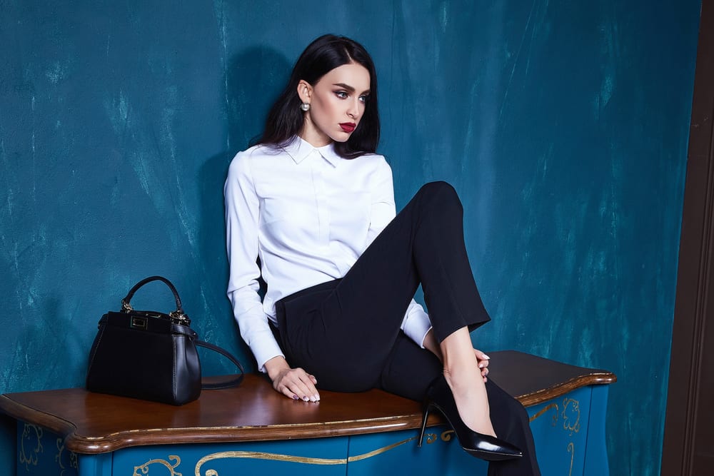 A woman wearing a pair of black tight dress pants and black stilettos.