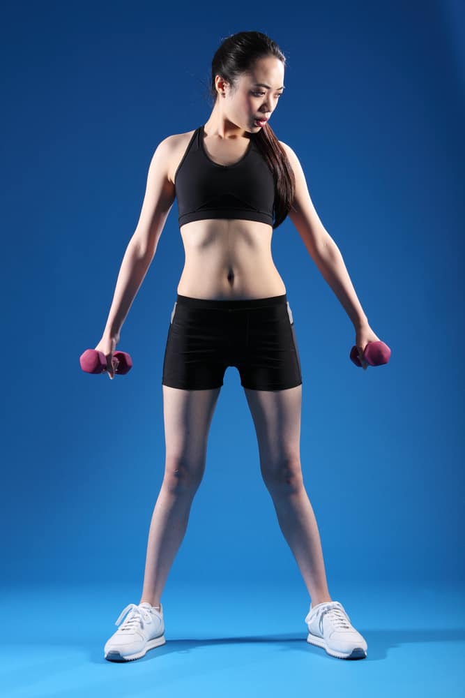 Girl in Lycra shorts working out with hand weights.