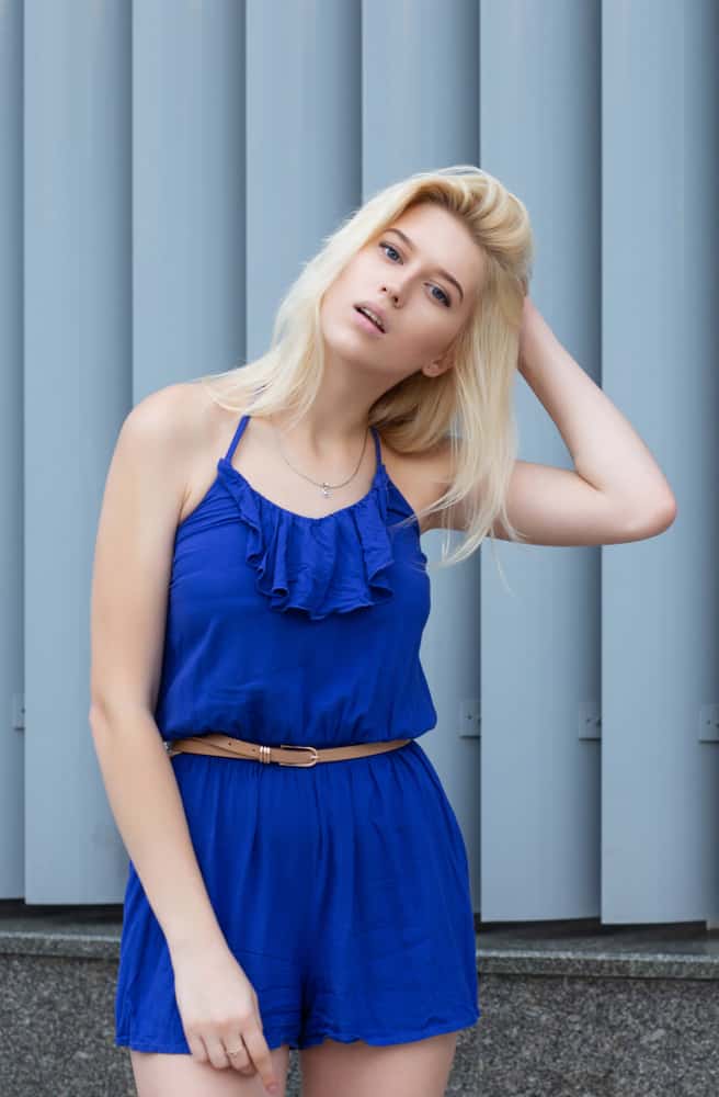 Model wearing a blue romper, poses against metal shutters.