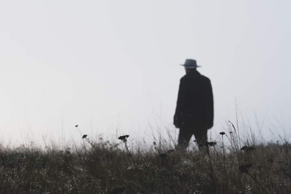 A man walking on a grass field wearing a fedora.