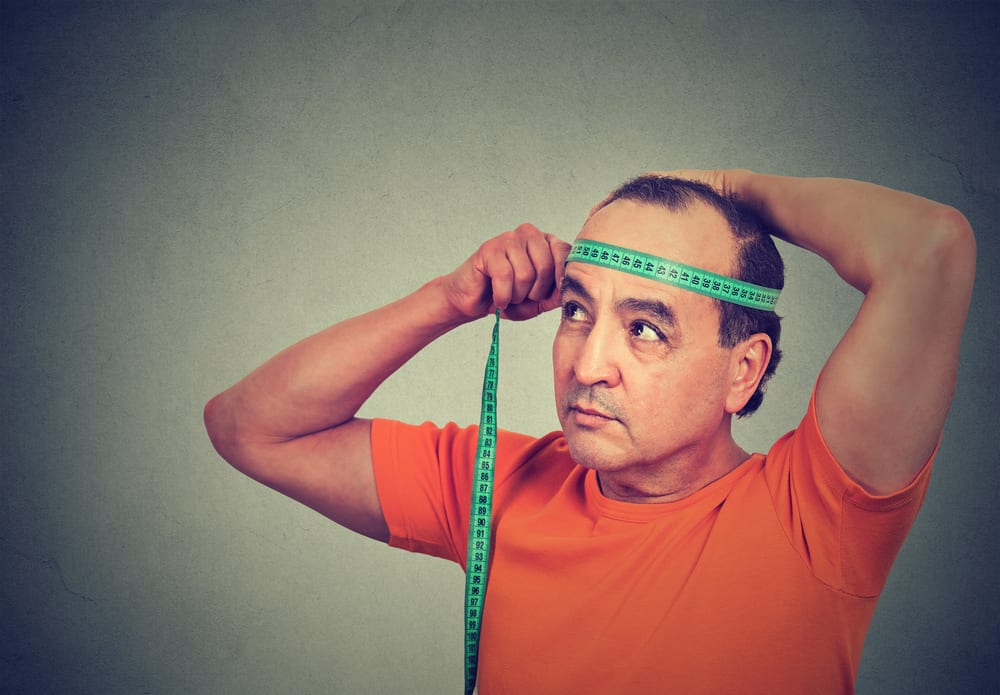 A close look at a man measuring his hat size with a measuring tape.
