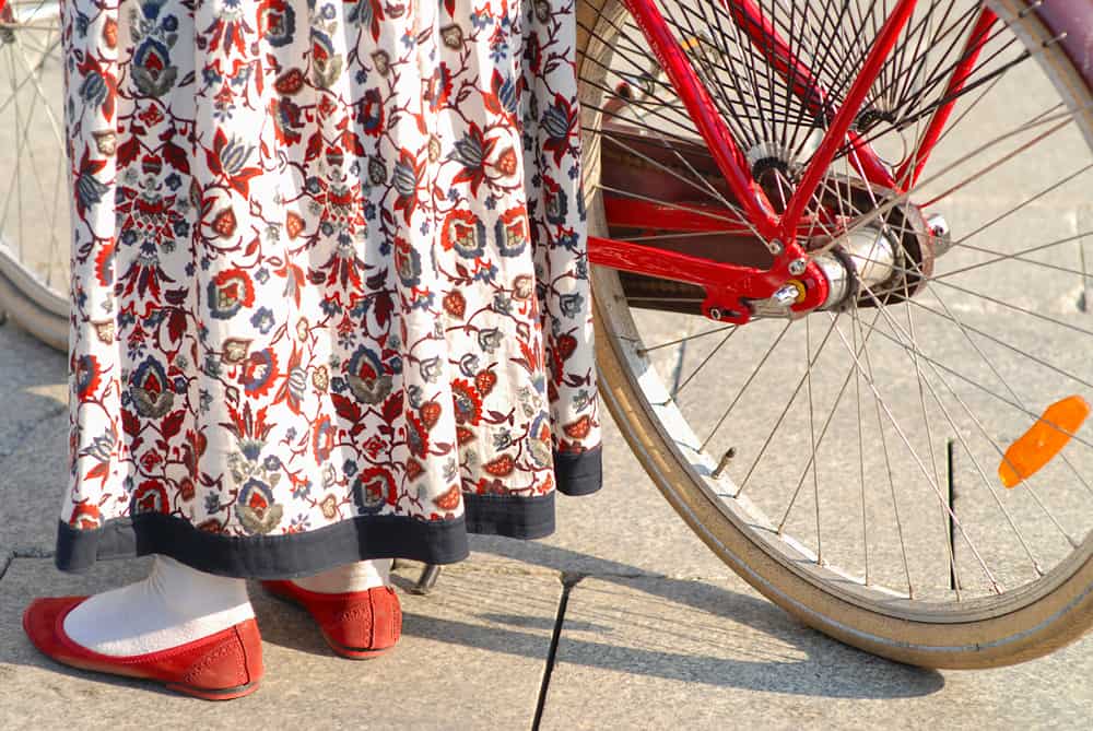 Woman walking her bike while wearing a long floral dress.