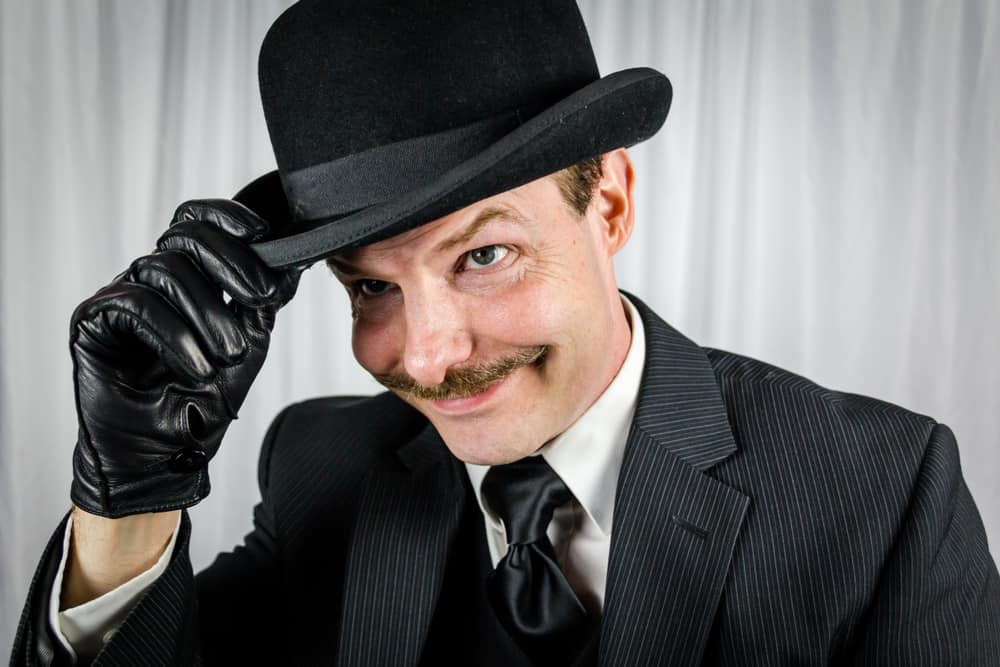 A man wearing a black pin-striped suit with a black bowler hat.