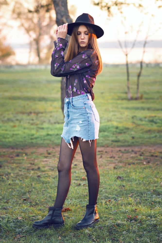 This is a close look at a woman wearing a ripped skirt jeans with her blouse and hat.