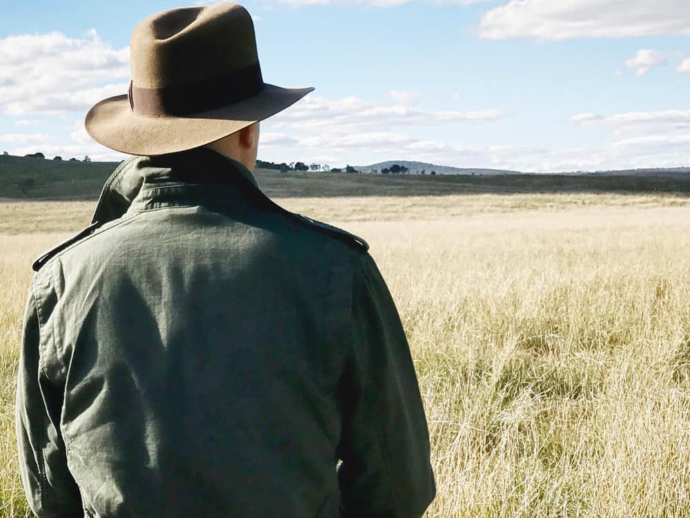 This is a close look at a man wearing a safari hat at a grass field.