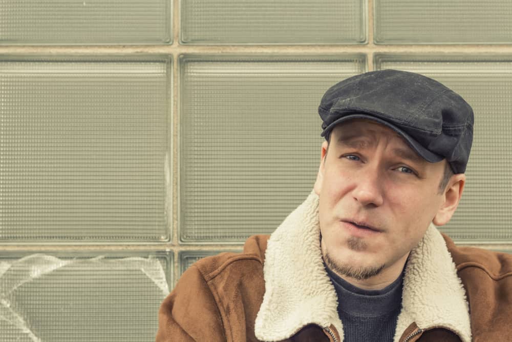 This is a close look at a man wearing an aviator jacket with his news-boy cap.