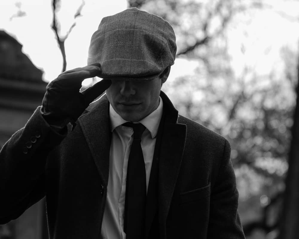 This is a close look at a man wearing a suit, leather gloves and an ivy cap.