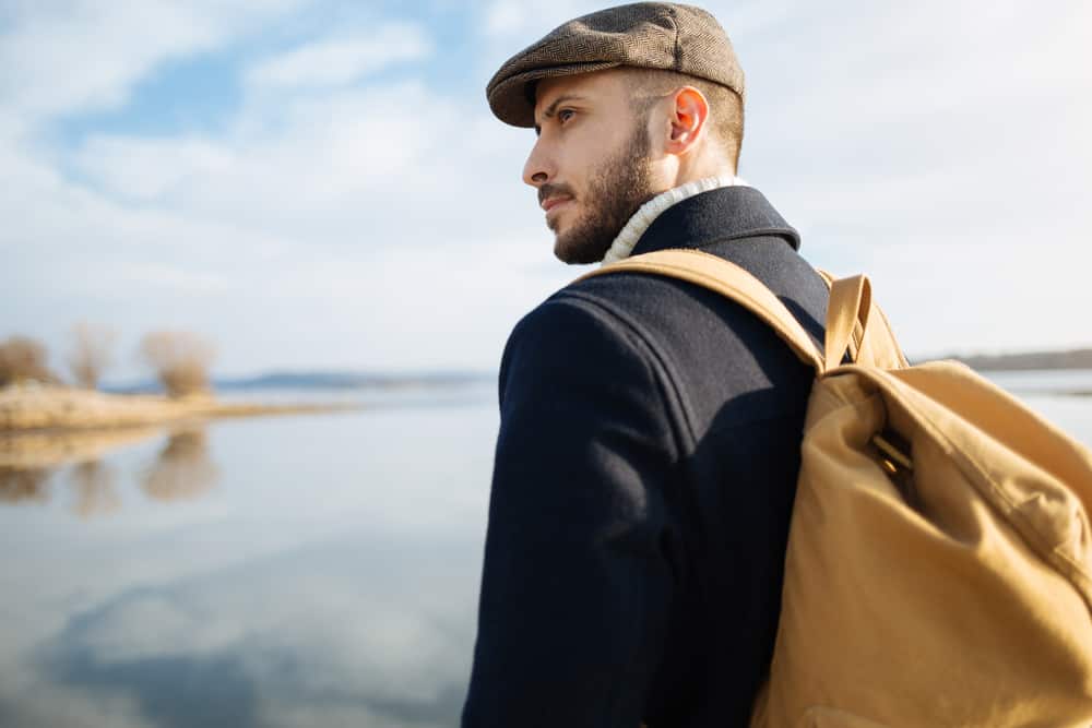 This is a traveling man wearing a jacket and an ivy cap while carrying his backpack.