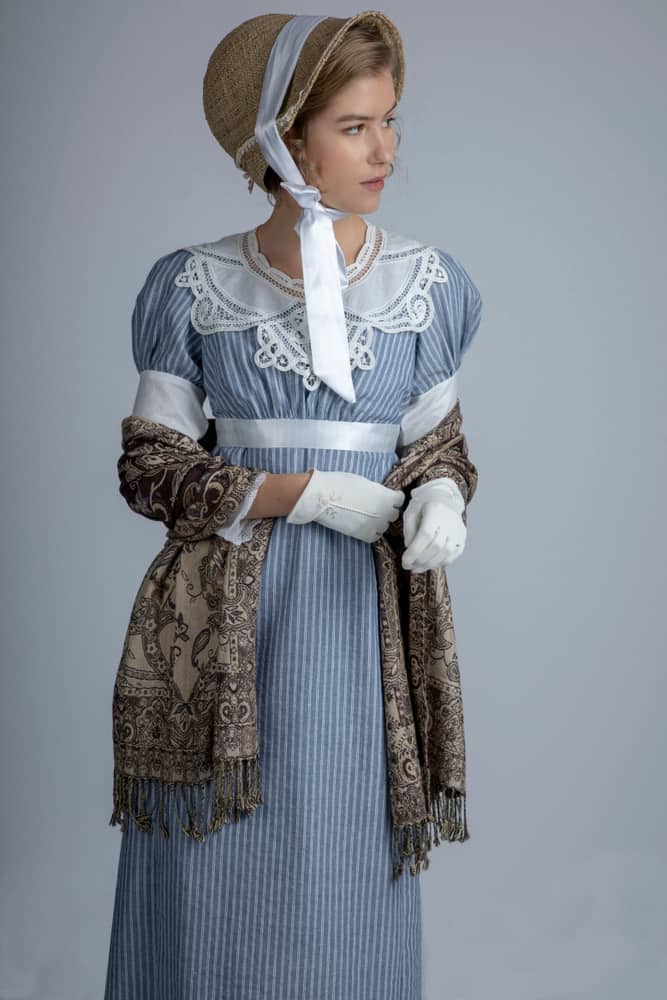 A woman wearing a blue vintage dress topped with a straw bonnet hat with ribbon.