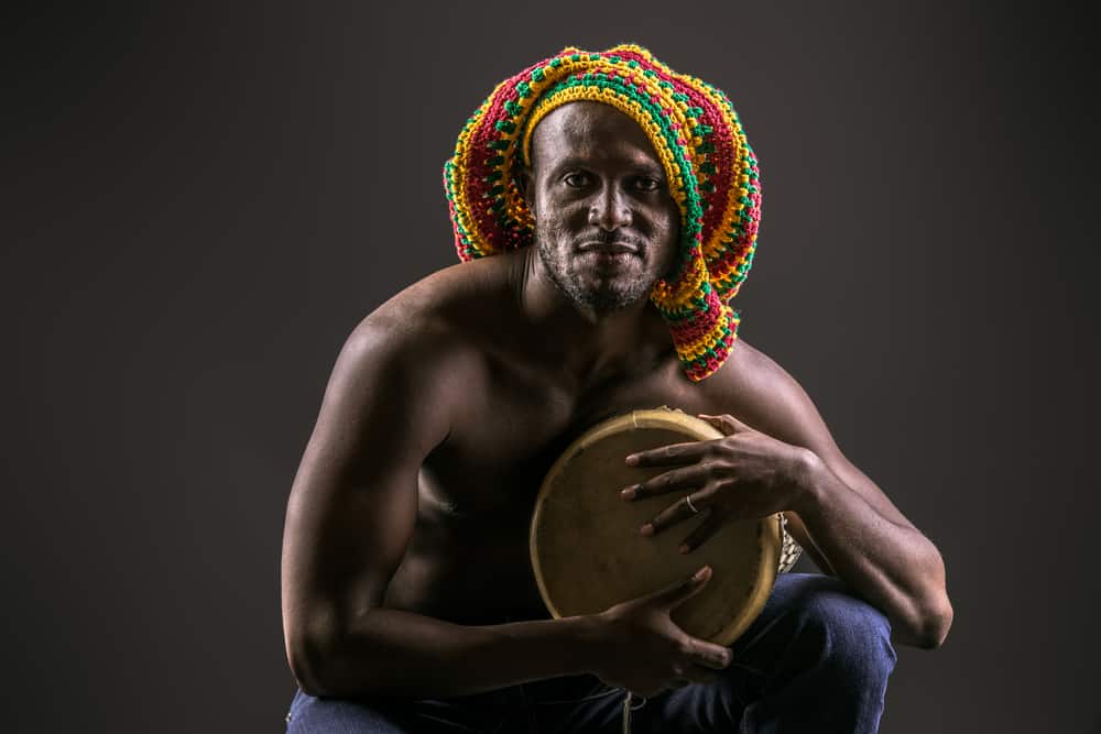 This is a rastafarian wearing a large rainbow knitted tam cap.